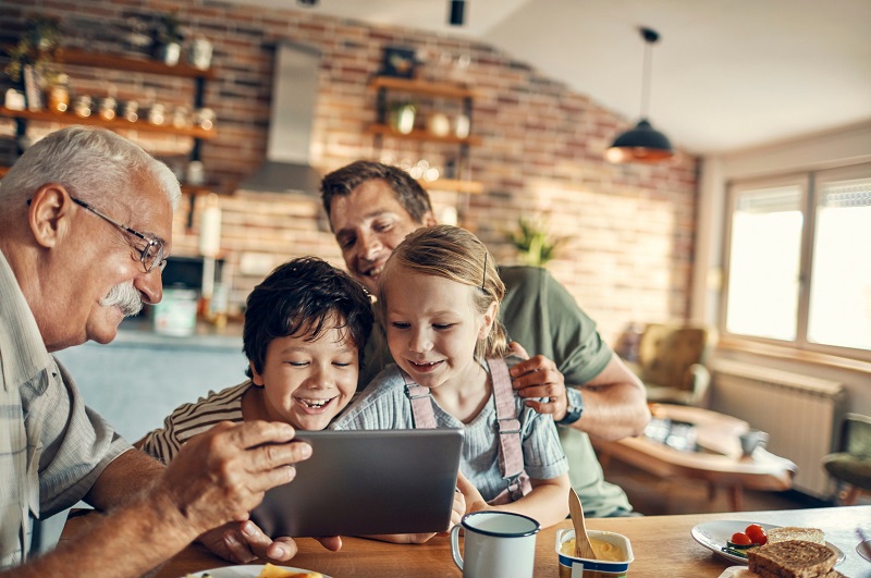 Grandfather enjoying a computer tablet with his grandkids and adult son in a multigenerational household