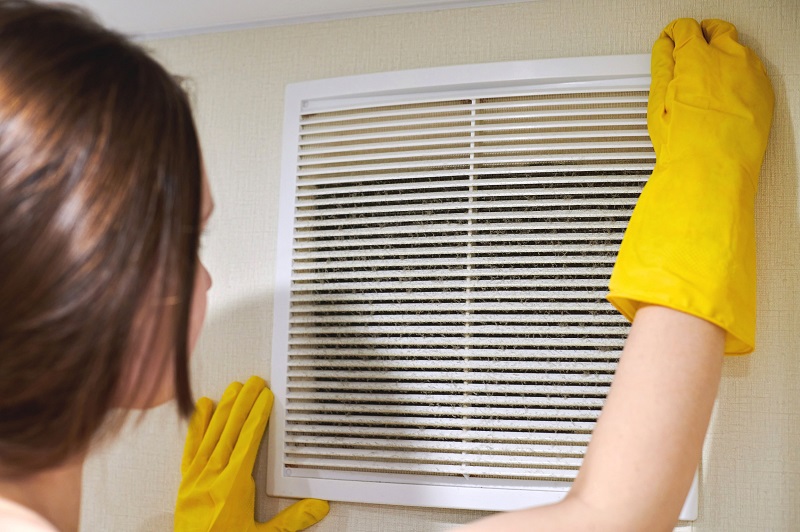 Woman cleaning an HVAC air vent with cleaning gloves.