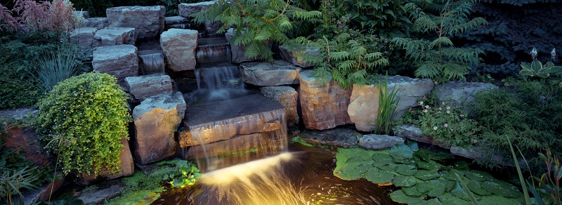 Large residential pond with stone waterfall with underwater landscape lighting