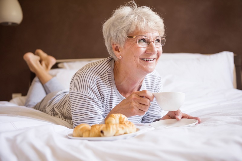 Elderly woman smiling in bed enjoying a cup of coffee for breakfast