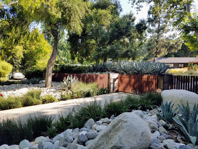 Home with driveway bordered with tall native grass with large rocks and gate