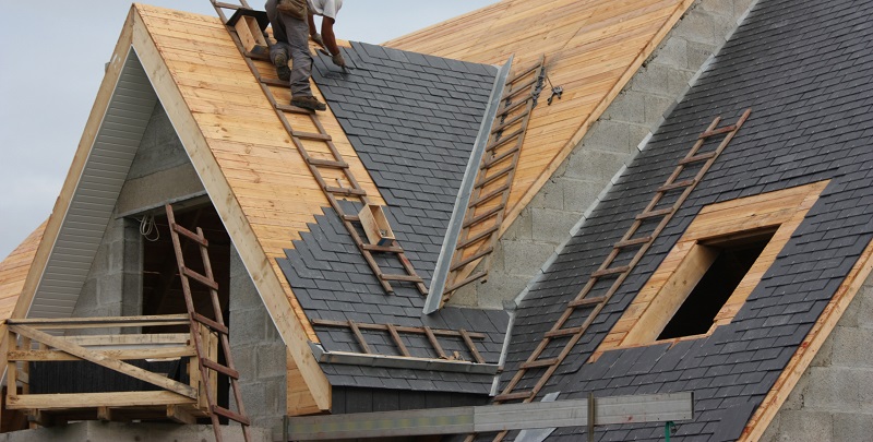 Professional roofer installing slate roof tiles on a new home construction