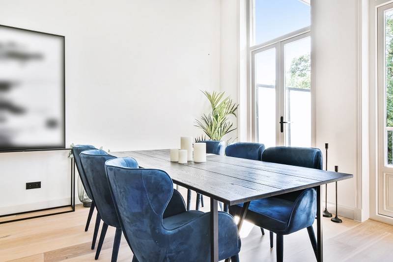 Blue chairs add to a bright dining room. Corner plant connects to the outdoors