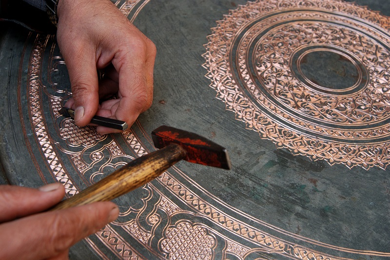 Skilled craftsman chiseling ornate details into a large copper tray