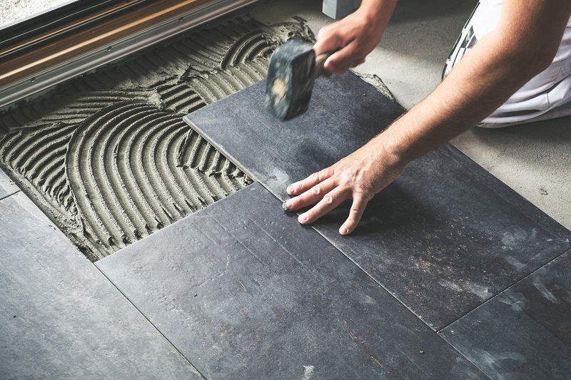 Contractor placing gray ceramic floor tiles in a kitchen