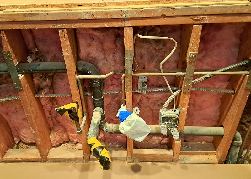 Exposed kitchen wall with plumbing, electrical wires, and gas lines