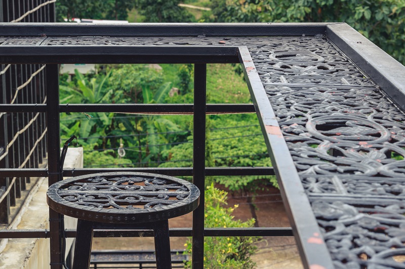 An ornate metal balcony with matching metal stool frames an enjoyable outdoor space with beautiful, peaceful views