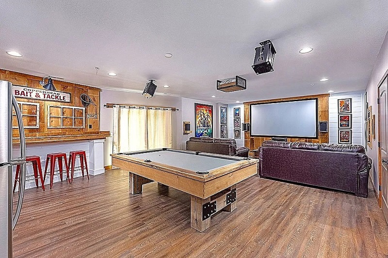 Large rec room with a billiard table, stools, refrigerator and an adjacent projector theater