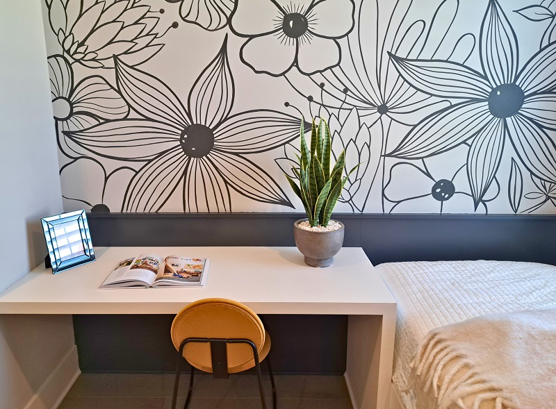 A workspace in a small bedroom featuring a biophilic wall treatment, wooden desk, and small house plant