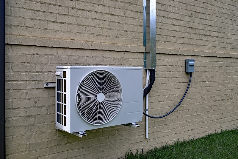 A modern mini-split heat pump attached to a brick wall of an older home, running to multiple indoor air handler units
