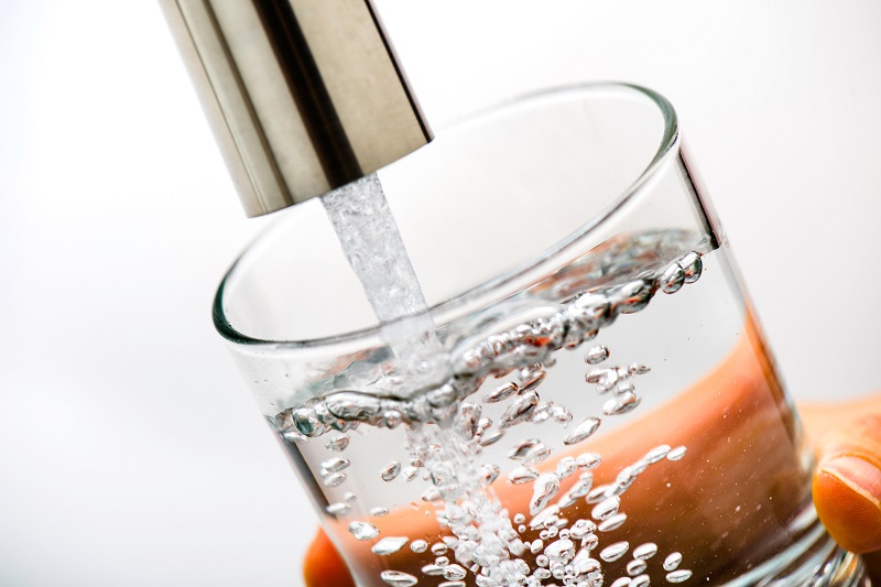 Clear glass of healthy water filtered from a whole house filtration systems served directly from a kitchen faucet.
