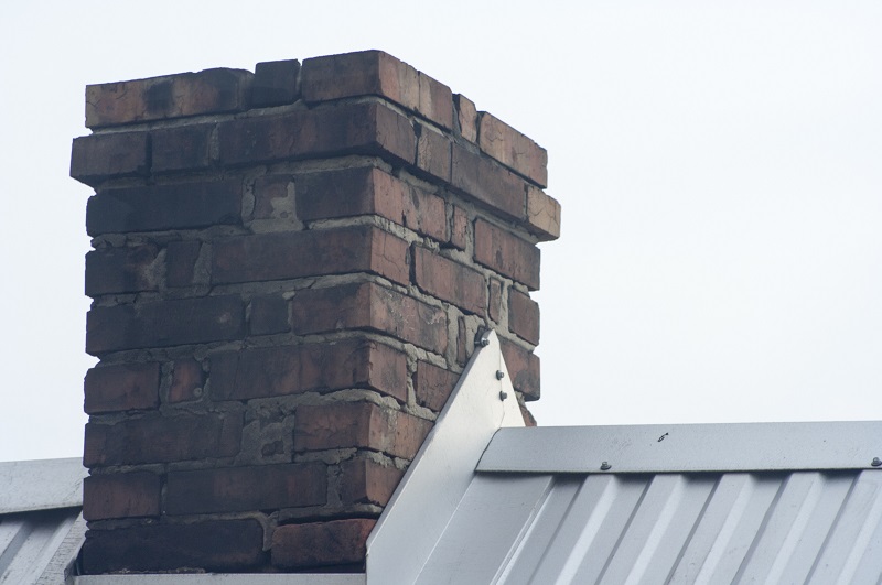 Home with old brick chimney with modern metal roof