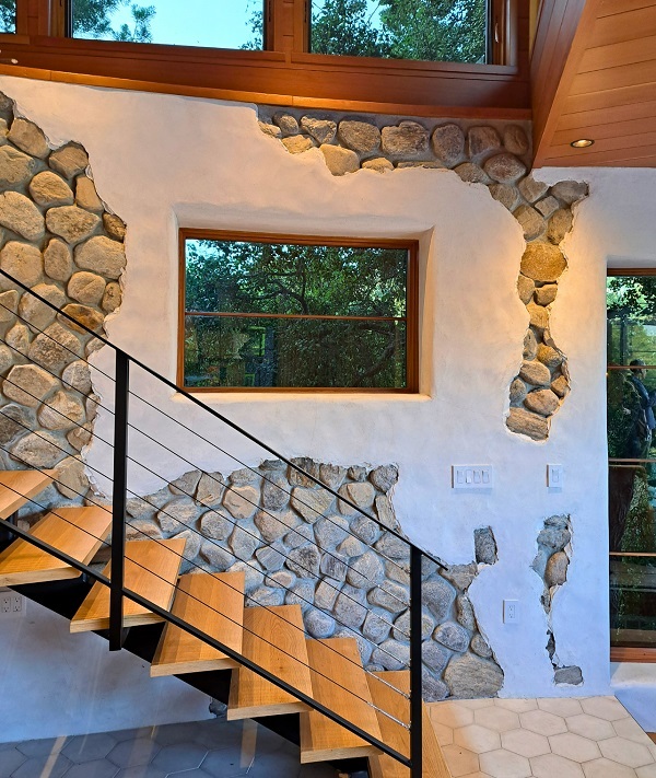 The curved stairway wall of Paraiso de Rocas Antiguas with biophilic views of the surrounding native greenery is symbolic of how well the home fits within the hillside