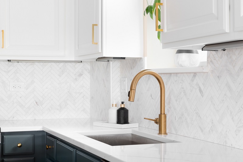 Gold kitchen faucet with herringbone tile backsplash