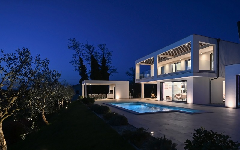 Modern white two-story villa with pool illuminated at night