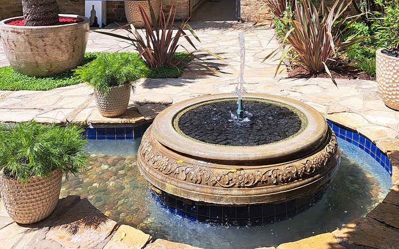 Working circular patio fountain in backyard patio with several potted plants