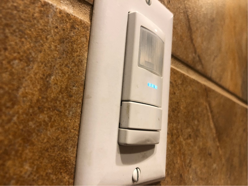 A wall-mounted passive infrared (PIR) occupancy sensor switch with a digital status indicator, acting as the eyes and ears of a room's lighting network.