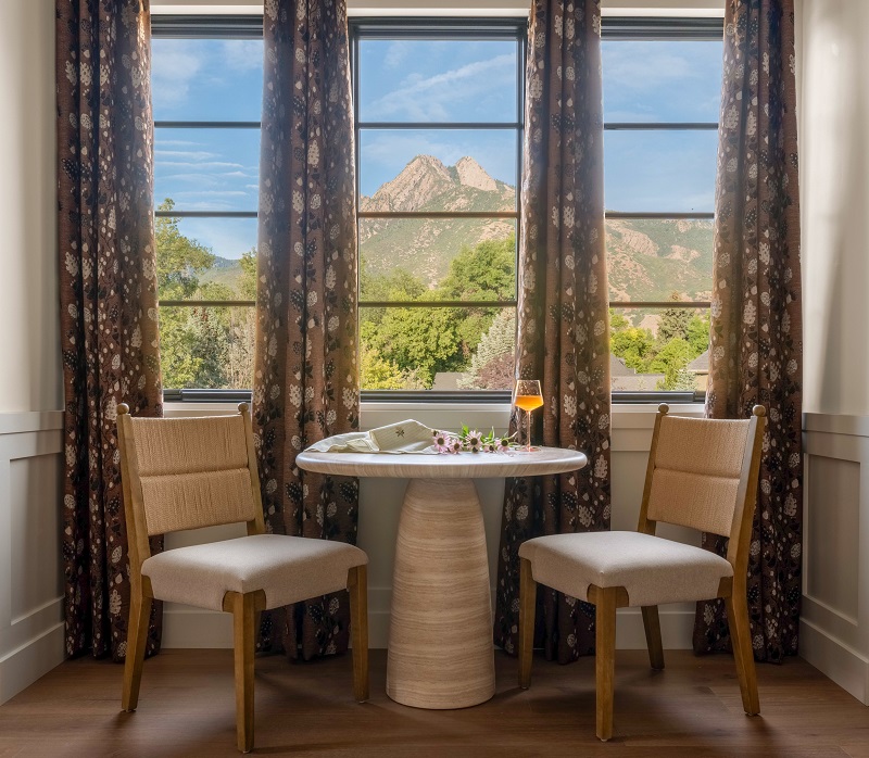 Small round dining table with two upholstered chairs in front of tall windows framing a mountain view
