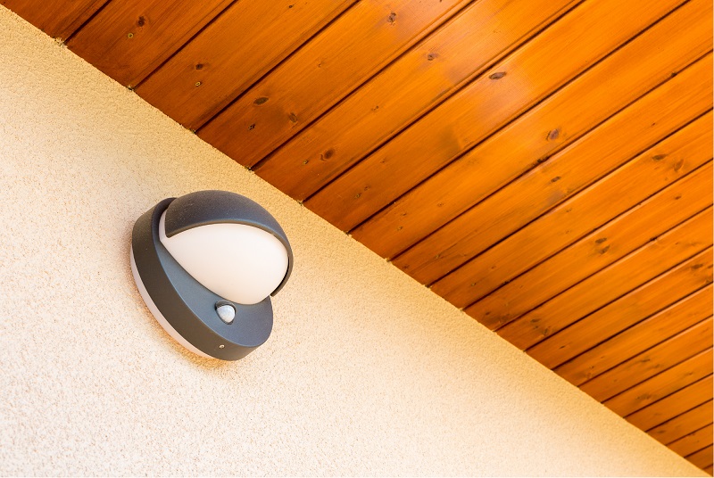An exterior architectural luminaire featuring an integrated sensor node to automatically balance fixture illumination against natural ambient daylight.